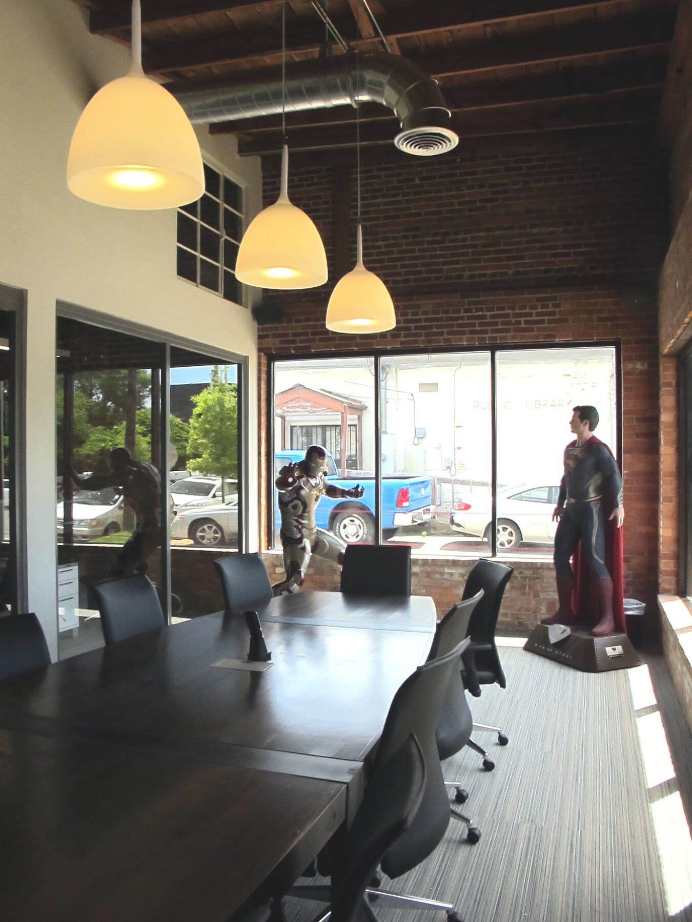 High ceilings with wooden beams exposed brick modern lighting and life-size comic book heroes lend personality to this inviting light-filled corner conference room 