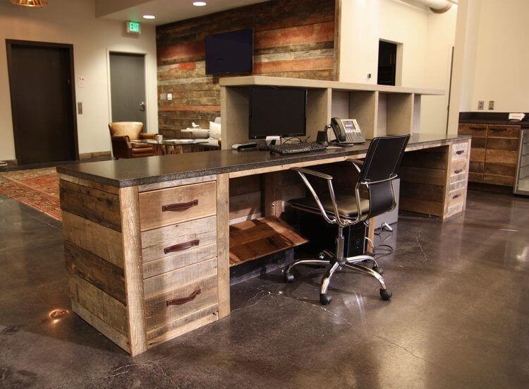 The reclaimed wood theme is woven throughout the space Here the receptionists reclaimed wood desk features some handsome leather handle pulls
