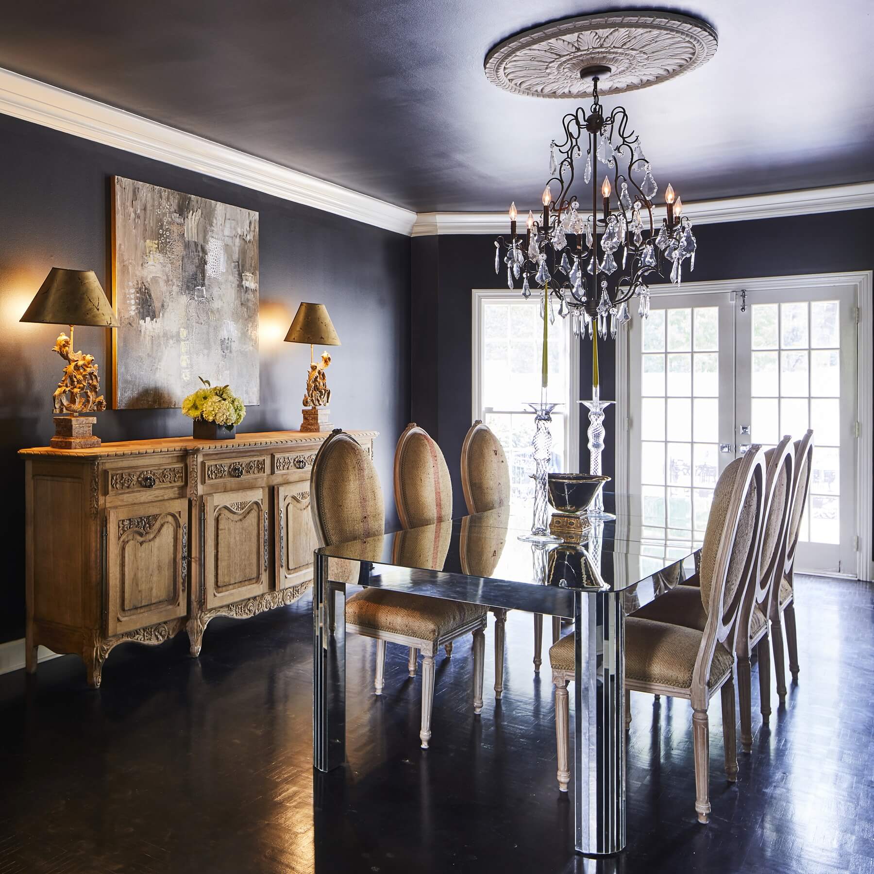 French-style chairs and an antique French sideboard flank the modern mirrored table in the dining room.