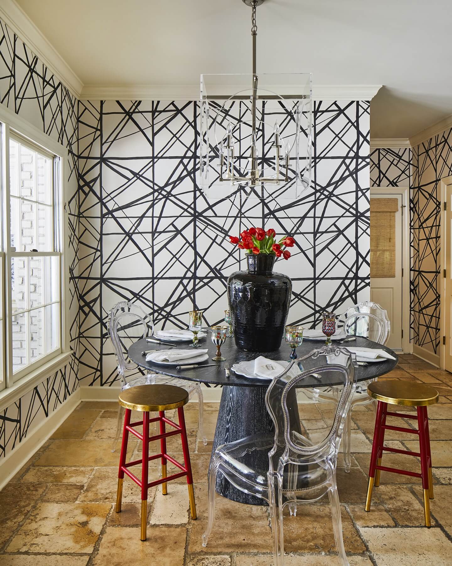 With its red gilded stools, acrylic ghost chairs, ghost chandelier, statement-making wallpaper and imposing modern table and centerpiece, this black-and-white dining nook is teeming with art-forward personality.