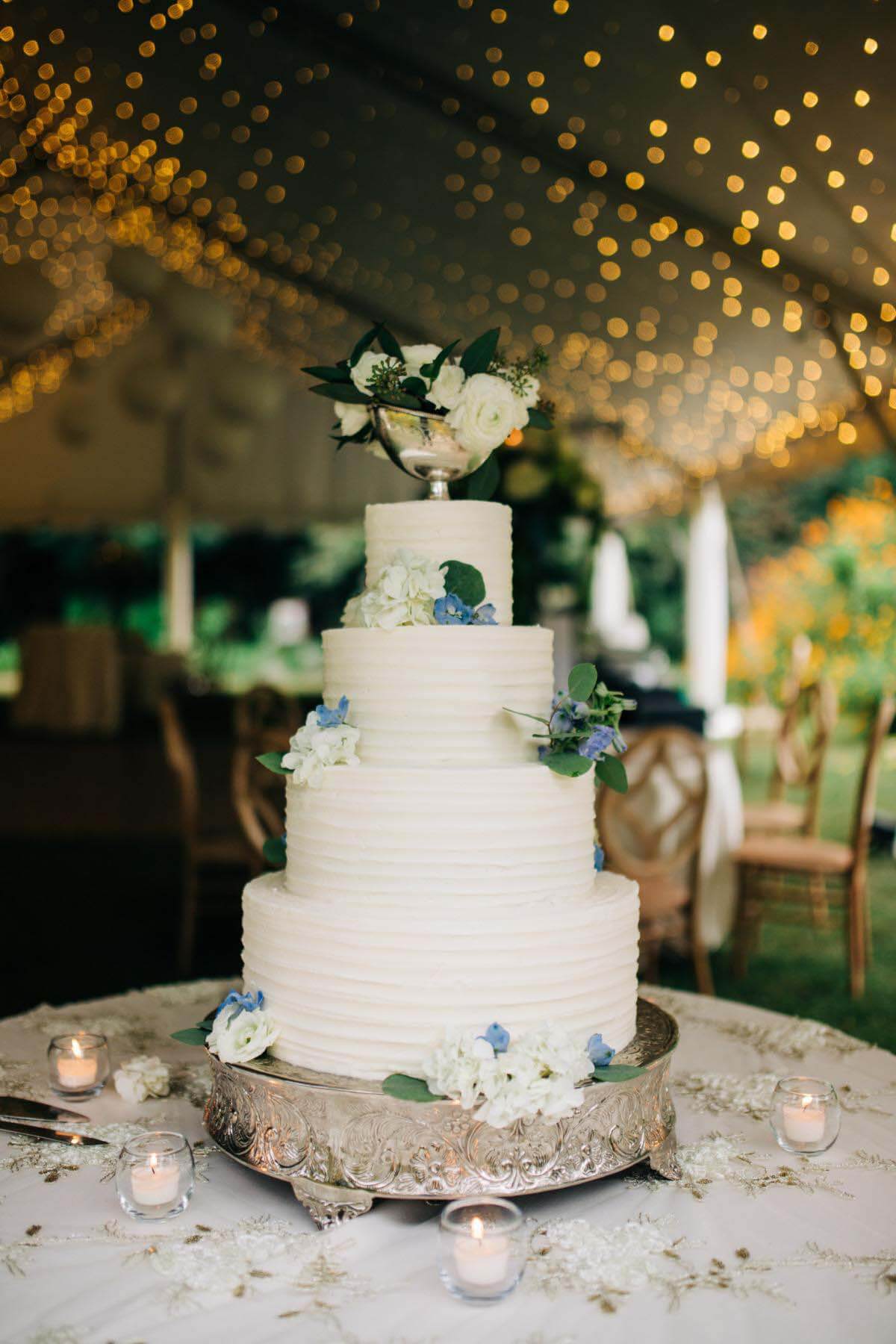 Gâteau de mariage à quatre niveaux sur un piédestal en argent orné de fleurs fraîches utilisées comme décor