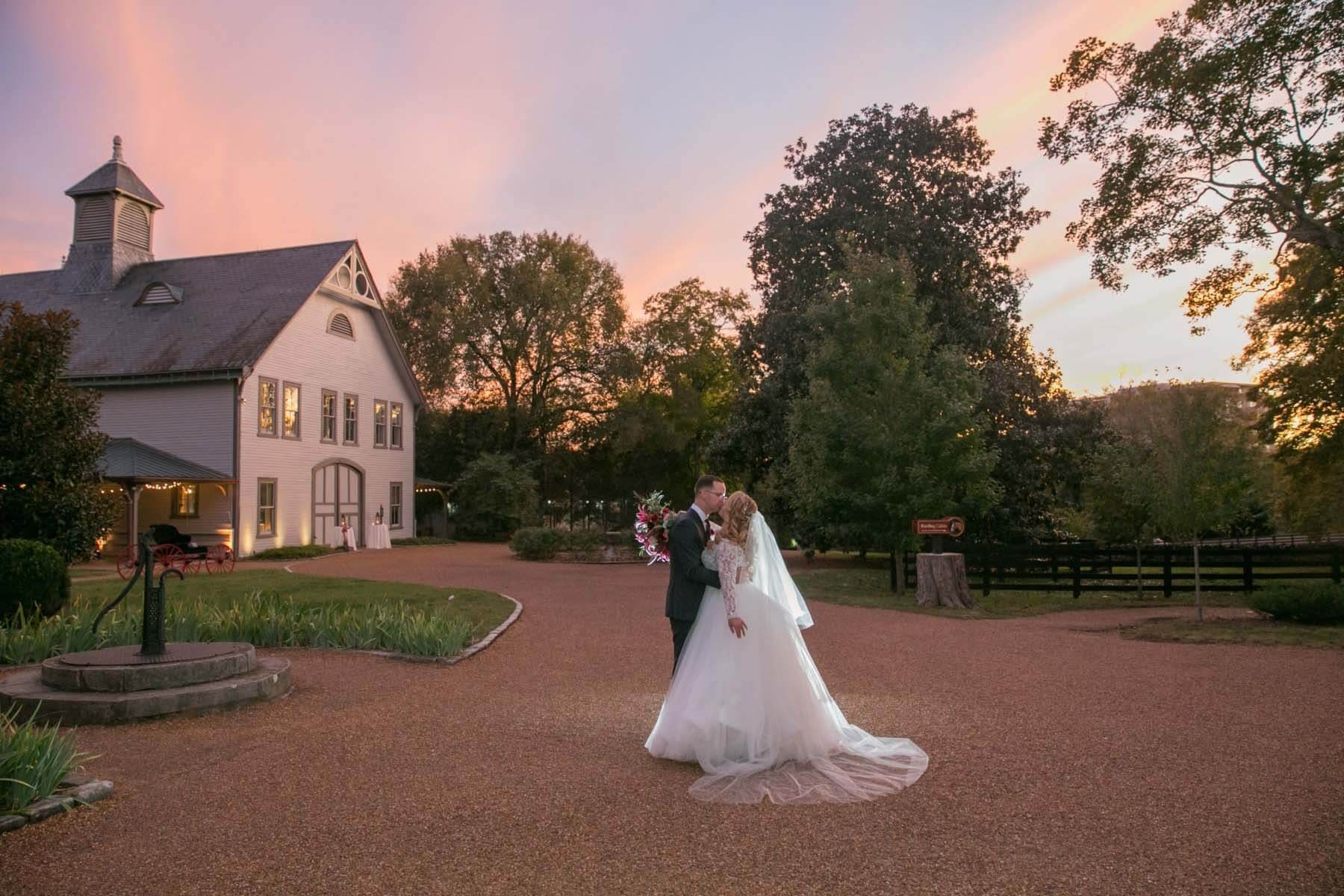 Les mariés s'embrassant au coucher du soleil à l'extérieur des écuries de Belle Meade Plantation