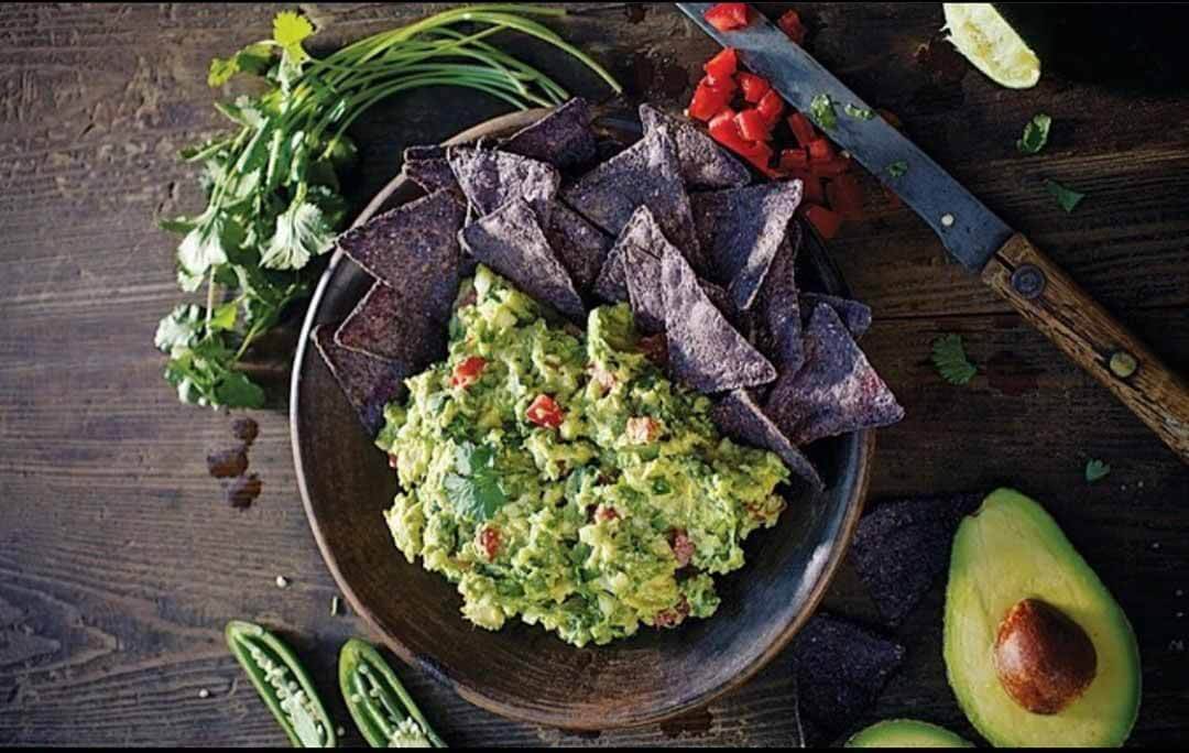 A bowl of guacamole with blue corn tortilla chips