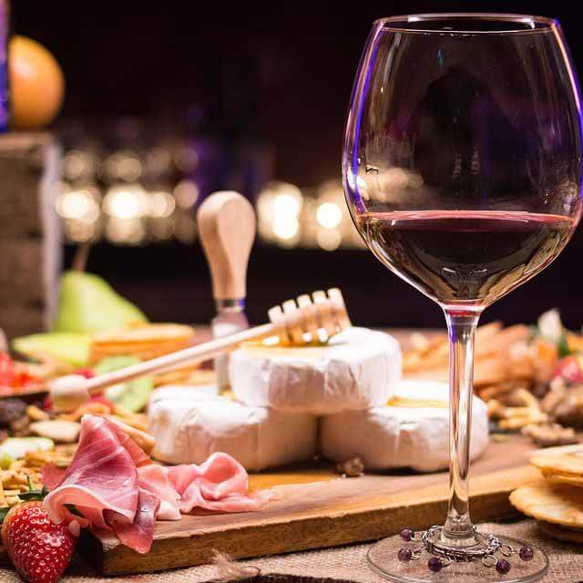 A glass of red wine with a plate of meat and cheese